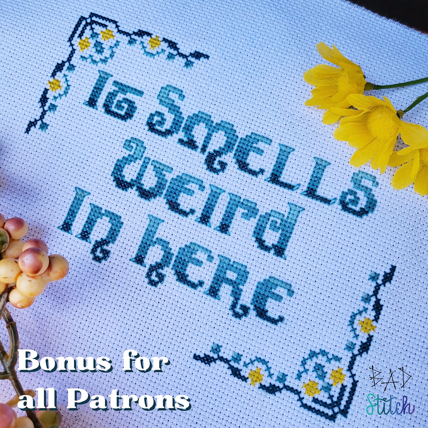 A cross stitch pattern on white fabric with lemon and vintage-style corner motifs and stitched text that says, "It smells weird in here."