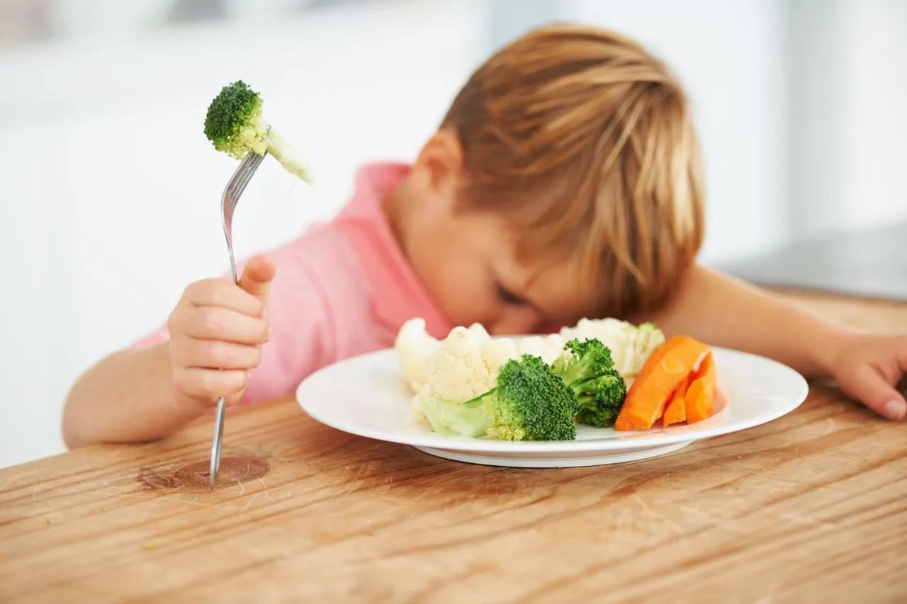 Boy sitting mournfully with a plate of vegetables and a forkful of broccoli. Boy sitting mournfully with a plate of vegetables and a forkful of broccoli.