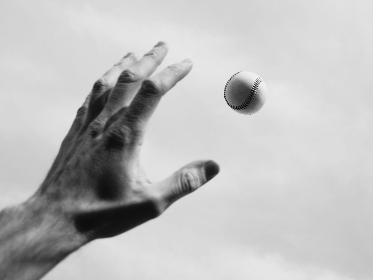 Black and white image of an outstretched left hand getting ready to catch a softball or baseball (depending on your country of origin!)