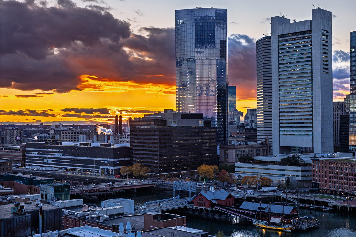 dramatic orange sunset behind boston seaport skyline reflecting off tall buildings