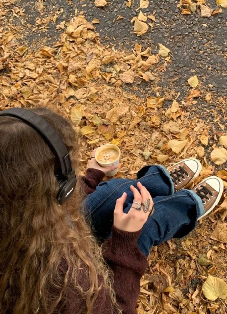 This may contain: a person with headphones on sitting in leaves