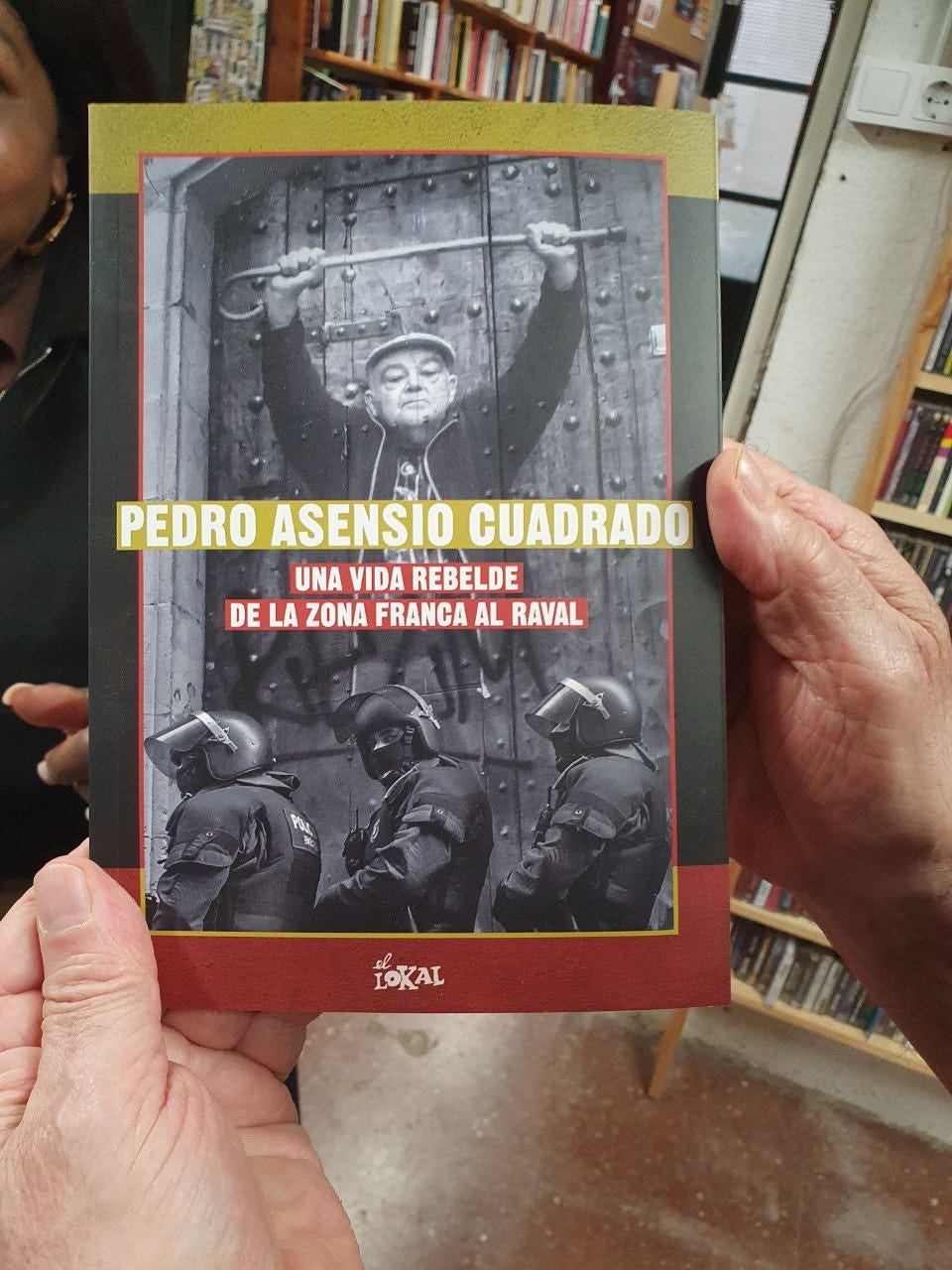 Two hands hold a book with the title "Pedro Asensio Cuadrado Una vida rebelde de la zona Franca al Raval"
