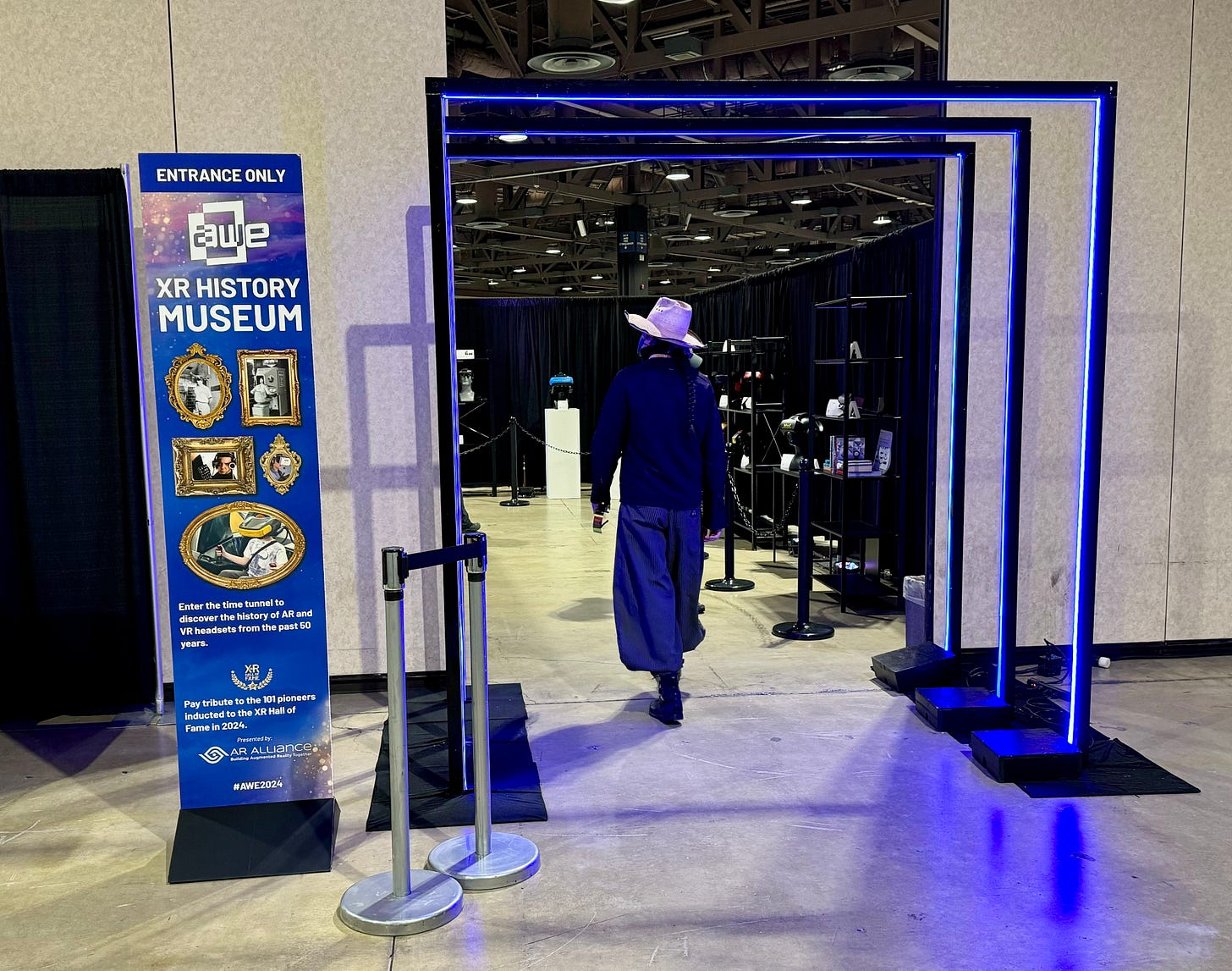 A conference attendee wearing a white hat walks through purple neon arches into the XR History Museum.