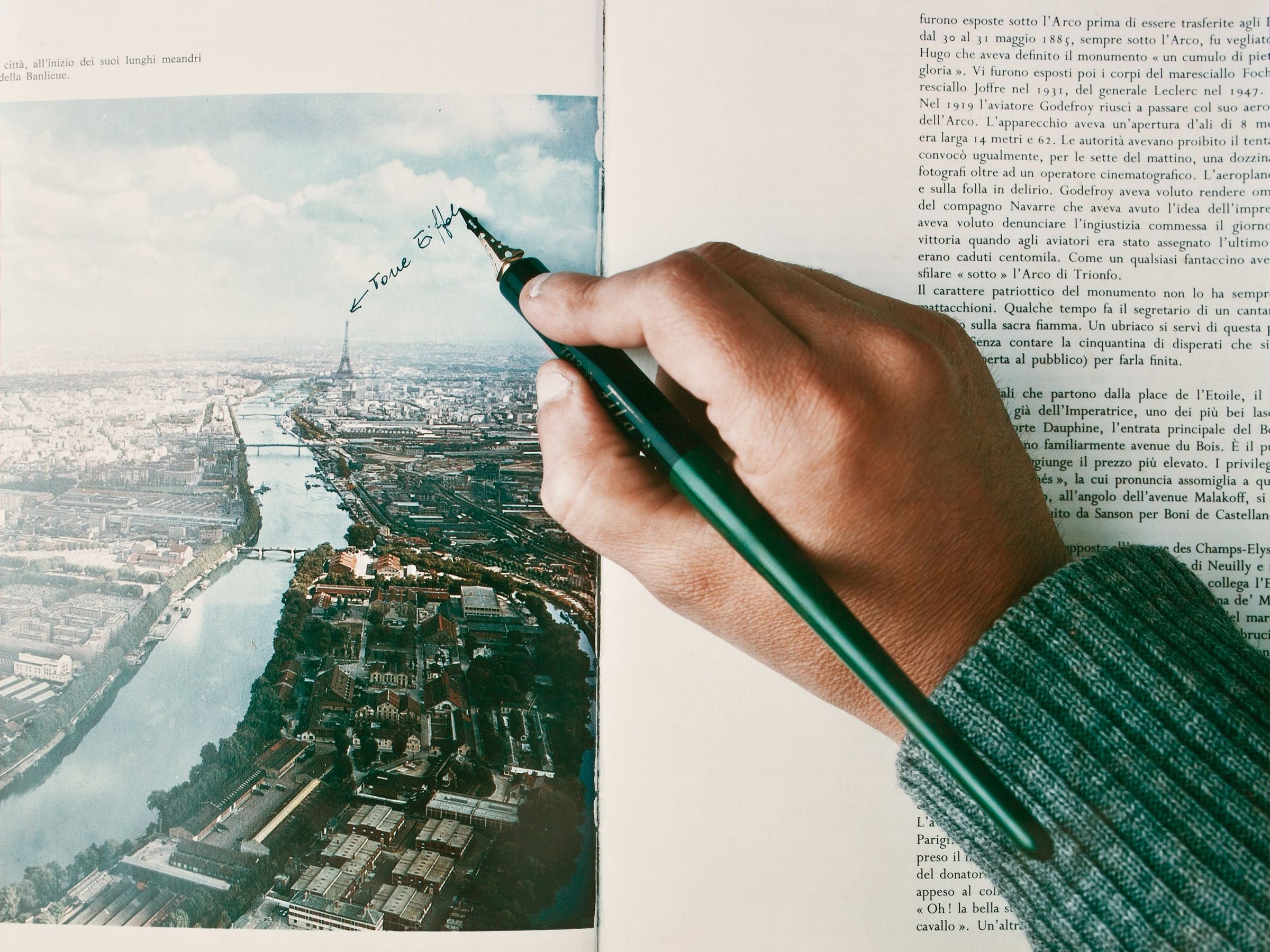 Polaroid by Luigi Ghirri. A hand rests over an open book displaying a photo of Paris labelling the Eiffel Tower with a pen