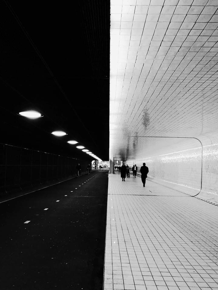 This may contain: black and white photograph of people walking in a subway station at night time with lights on
