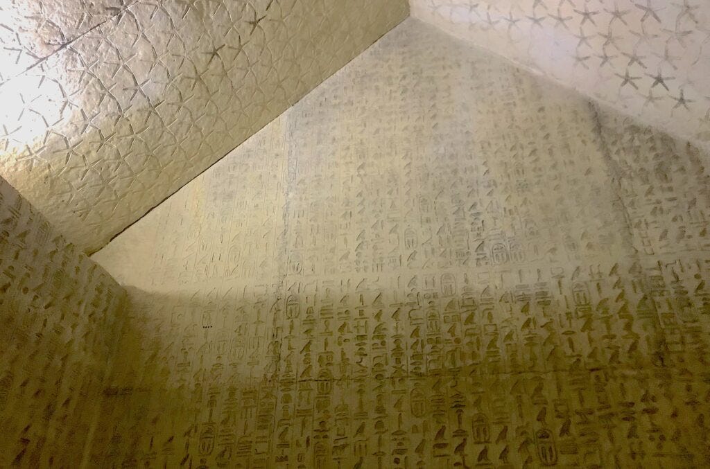 Photographed from below, a large beige stone wall and ceiling are covered in various etchings and symbols. Photographed from below, a large beige stone wall and ceiling are covered in various etchings and symbols.