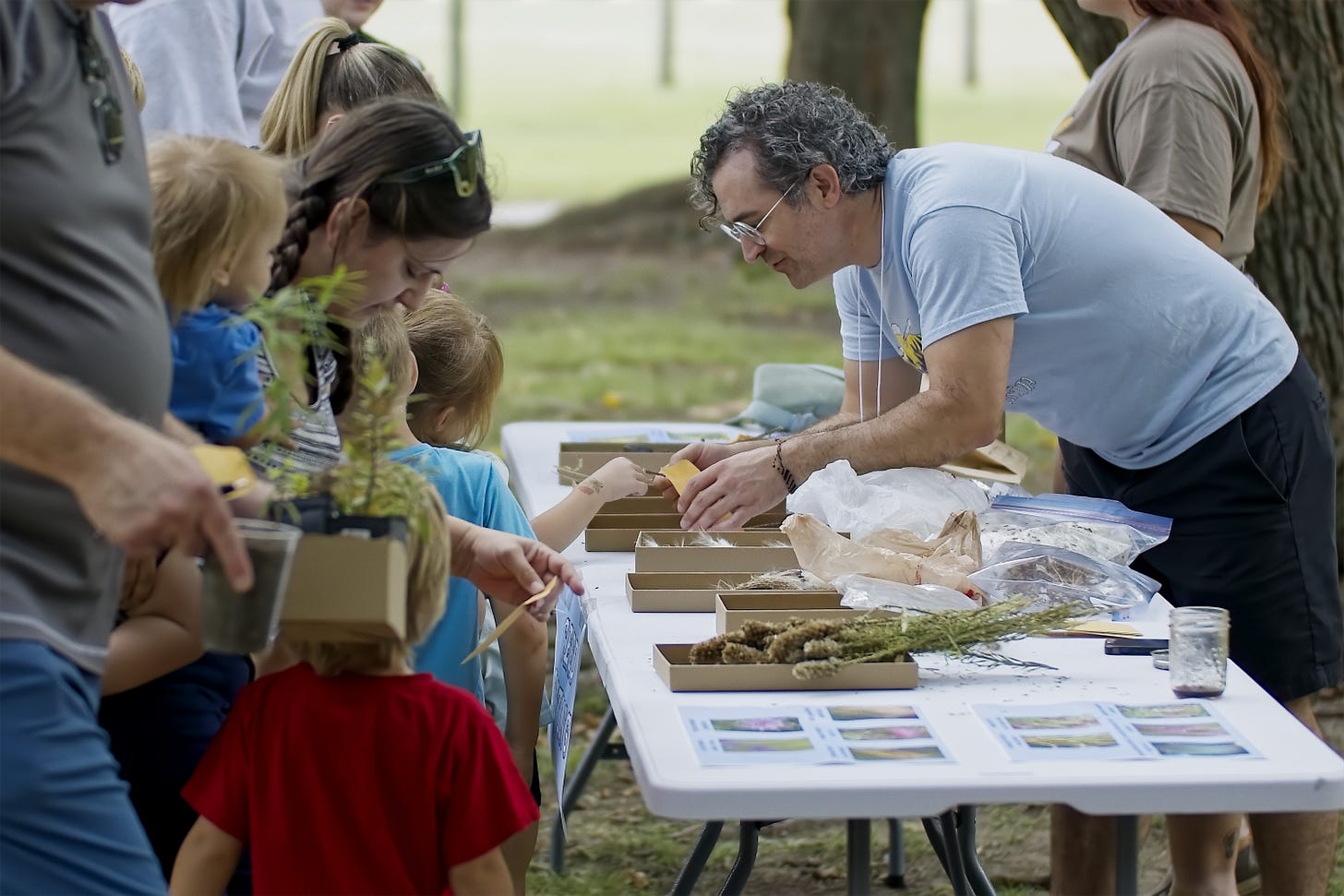 A family sorts through seeds at a table with help from volunteer Adam.