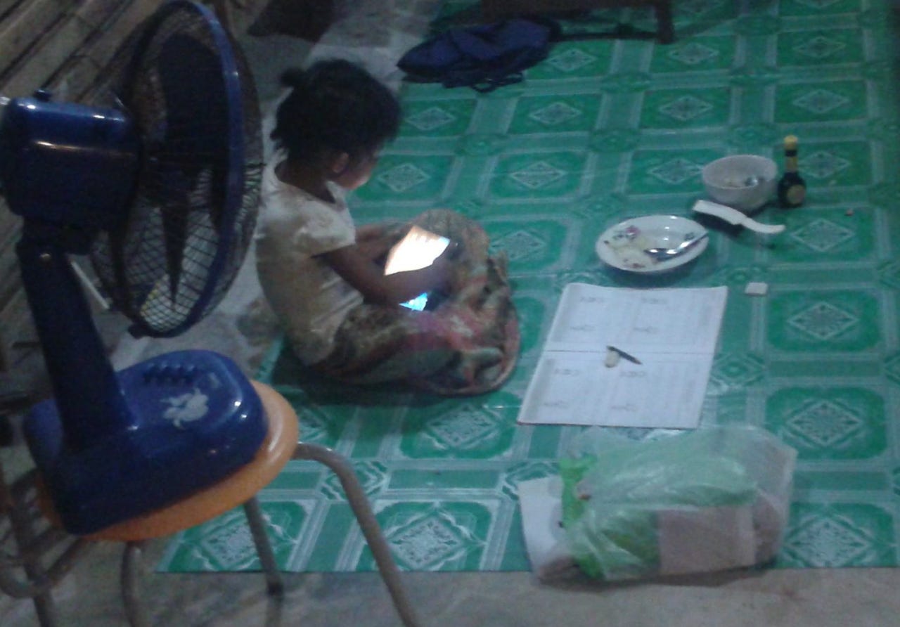 Child sitting on the floor next to her meal and homework. She is using a low cost Android OS based tablet computer. The image was taken at Ko Lanta Thailand.