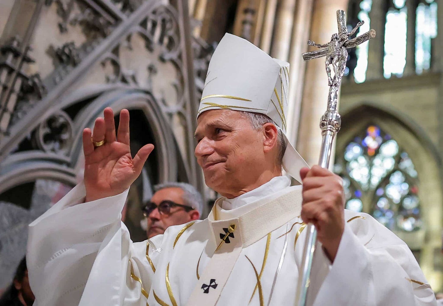 Pope Leo XIV waves while holding his pastoral staff inside a Gothic cathedral Pope Leo XIV waves while holding his pastoral staff inside a Gothic cathedral