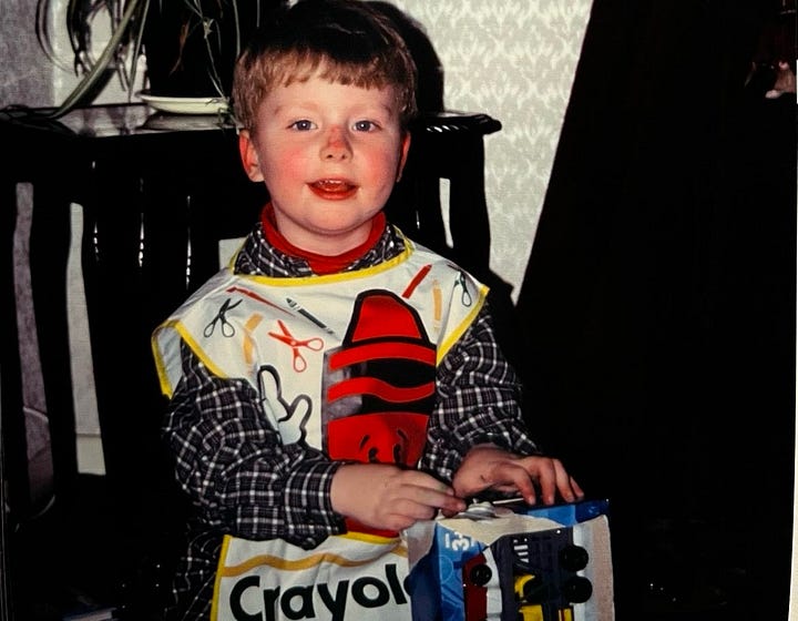 Photo of James as a young child wearing a crayola apron, next to it is a school christmas play poster.