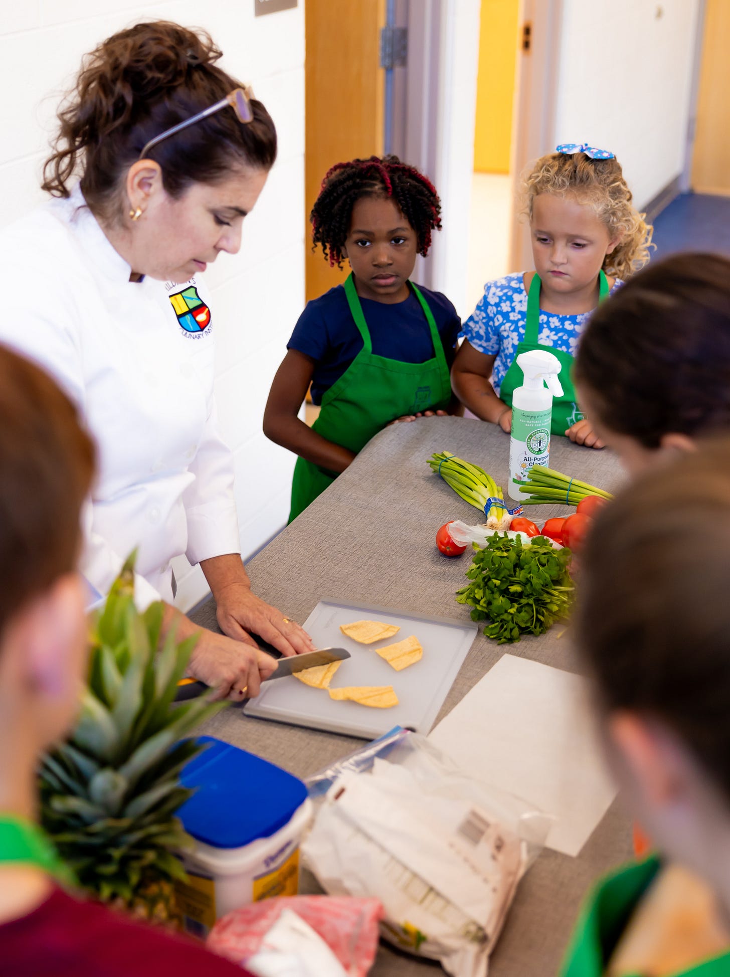 Chef demonstrating to children how to use a knife and cutting board during a cooking class