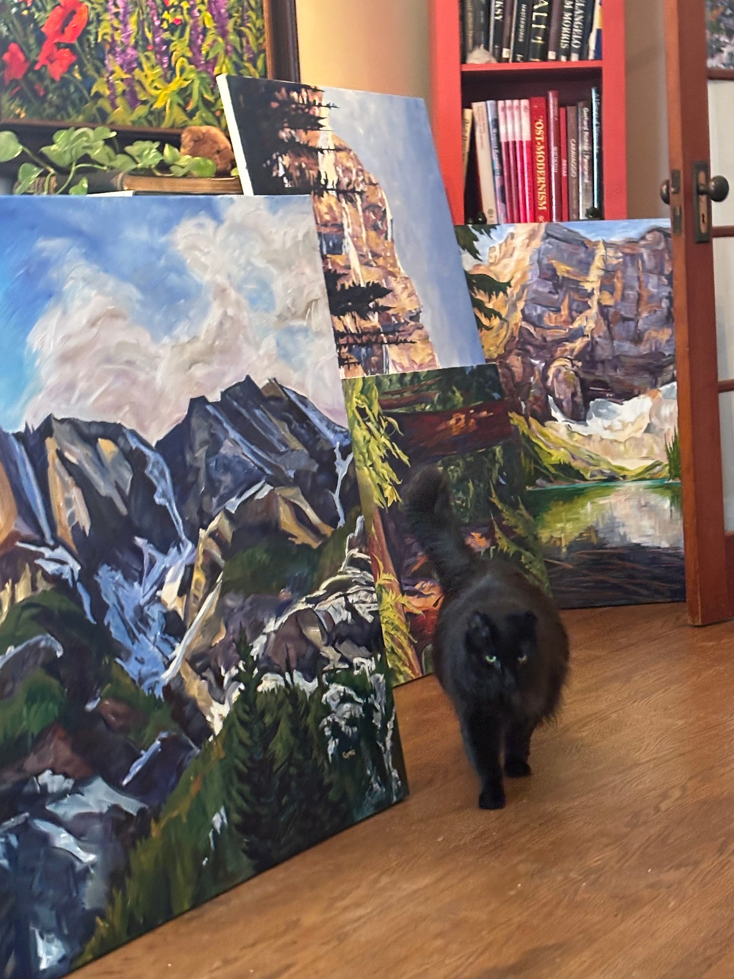 a photo of Tina the cat walking by Caprice's oil paintings.