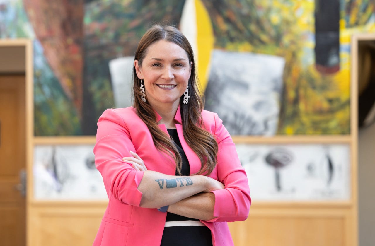 Image of Secretary Fagan wearing vote earrings while showing her not tattoo.