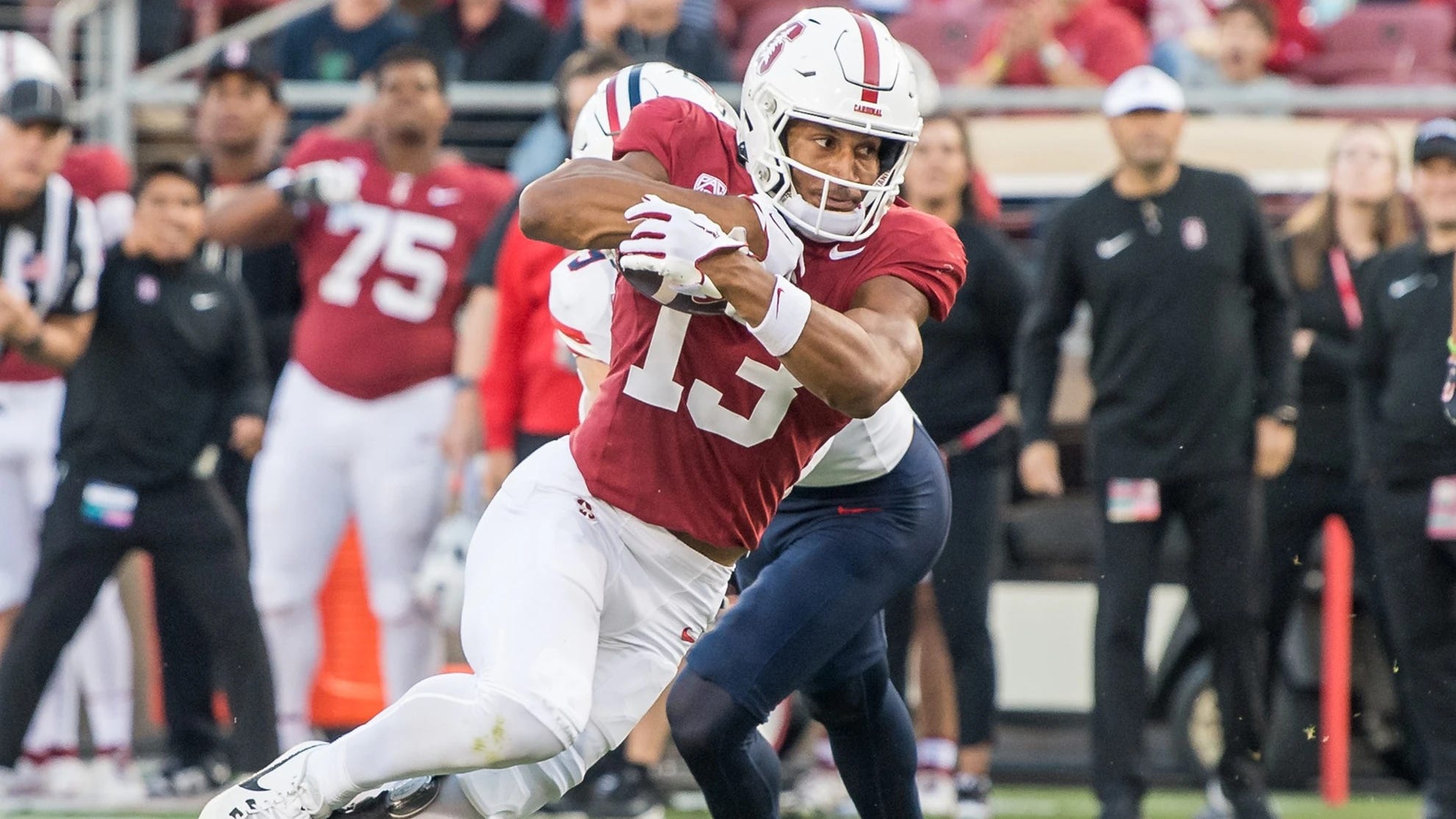 A football player carries a football while running up the field as a defender attempts to stop his during a Stanford Cardinal football game. A football player carries a football while running up the field as a defender attempts to stop his during a Stanford Cardinal football game.