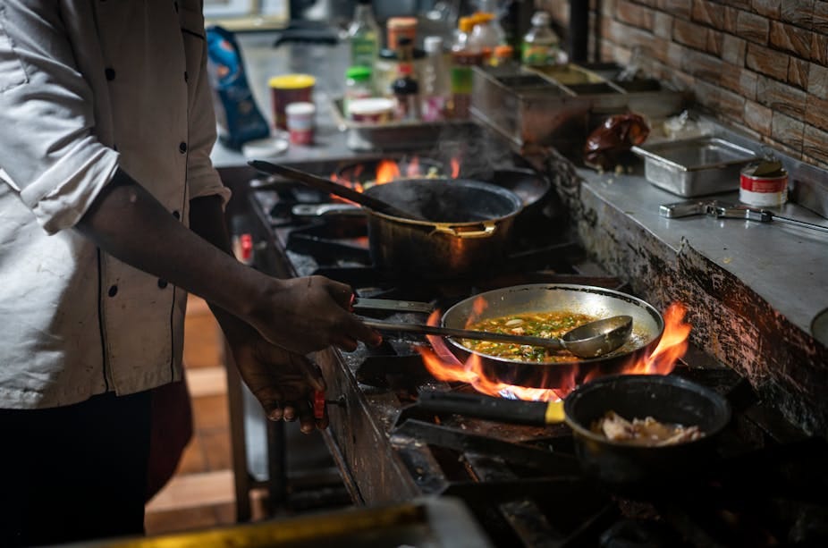 A man cooks four pans of food over gas A man cooks four pans of food over gas
