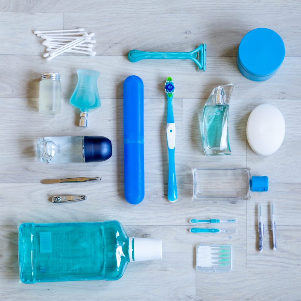 A photo looking down at a counter filled with hygiene products that are nicely lined up in rows. The products are in shades of blue and white. There are cotton buds, deodorant, toothbrushes, a razor, nail clipper and floss.