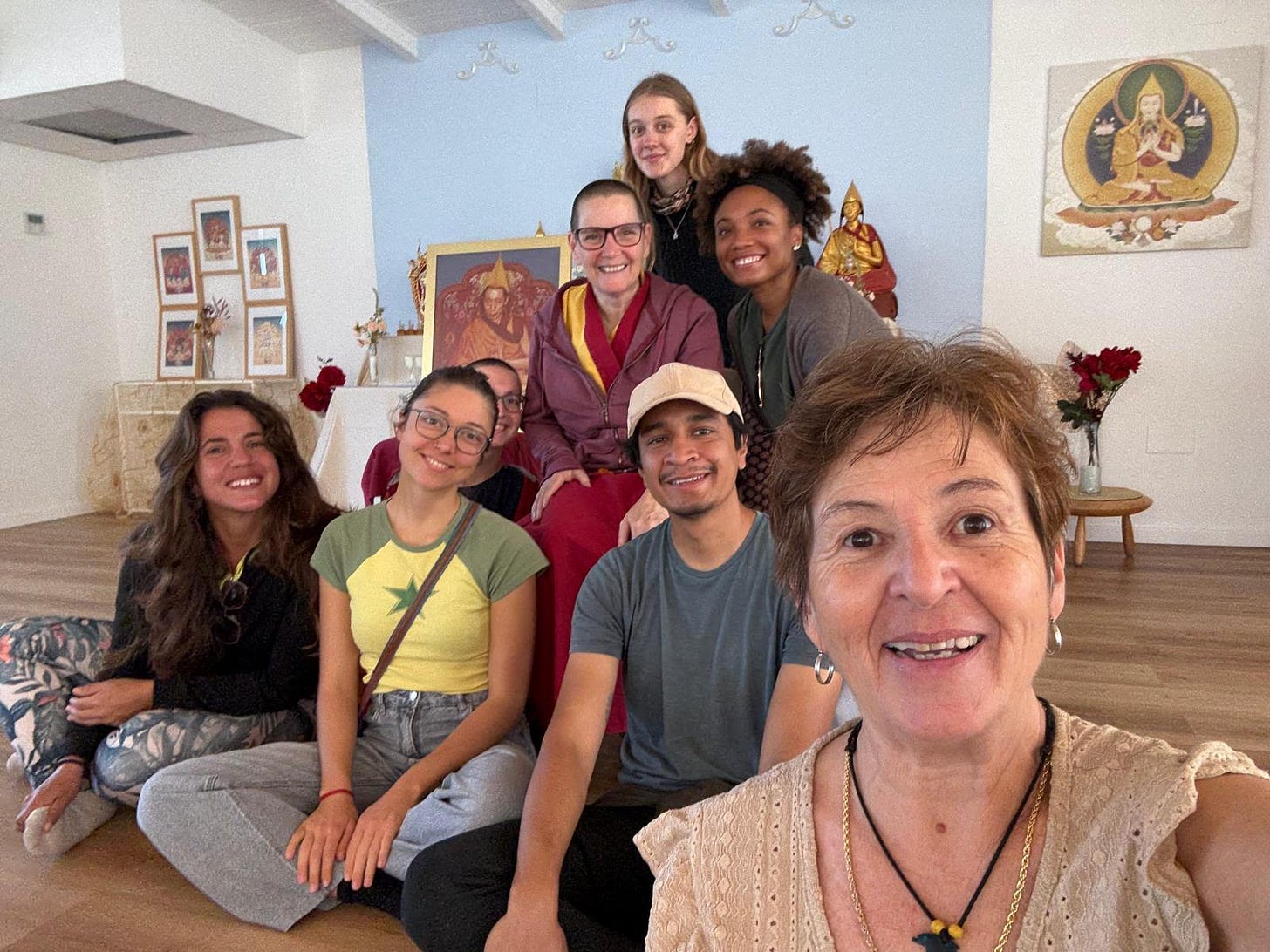 Volunteers gathered with a Buddhist nun teacher inside a meditation room, surrounded by thangka paintings and altar decorations. Volunteers gathered with a Buddhist nun teacher inside a meditation room, surrounded by thangka paintings and altar decorations.