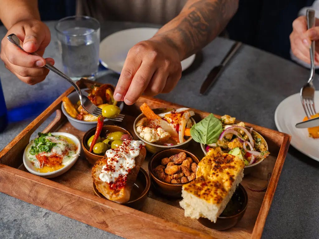 A tray of small bowls full of olives, pickled vegetables, nuts and bread.