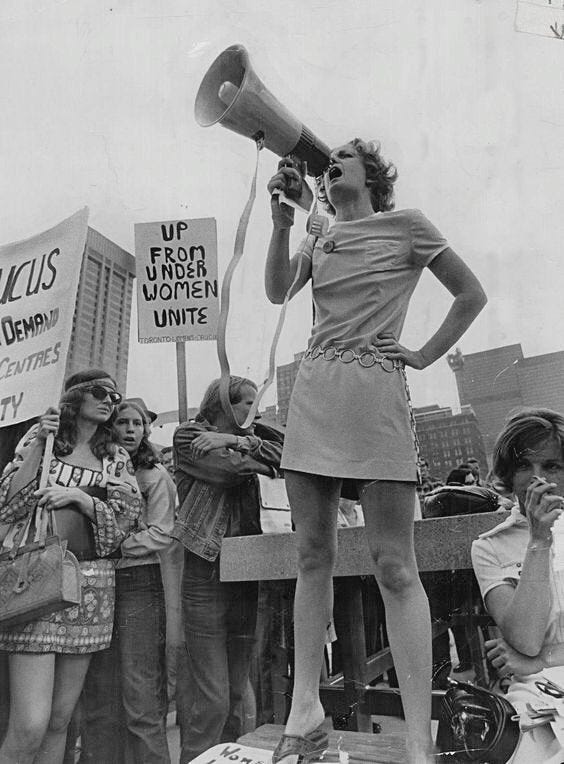 This may contain: a black and white photo of a woman speaking into a megaphone in front of people holding signs