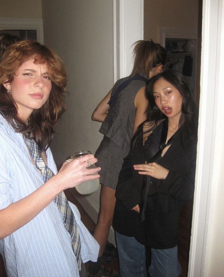This may contain: two women standing next to each other in front of a mirror with one woman holding a glass