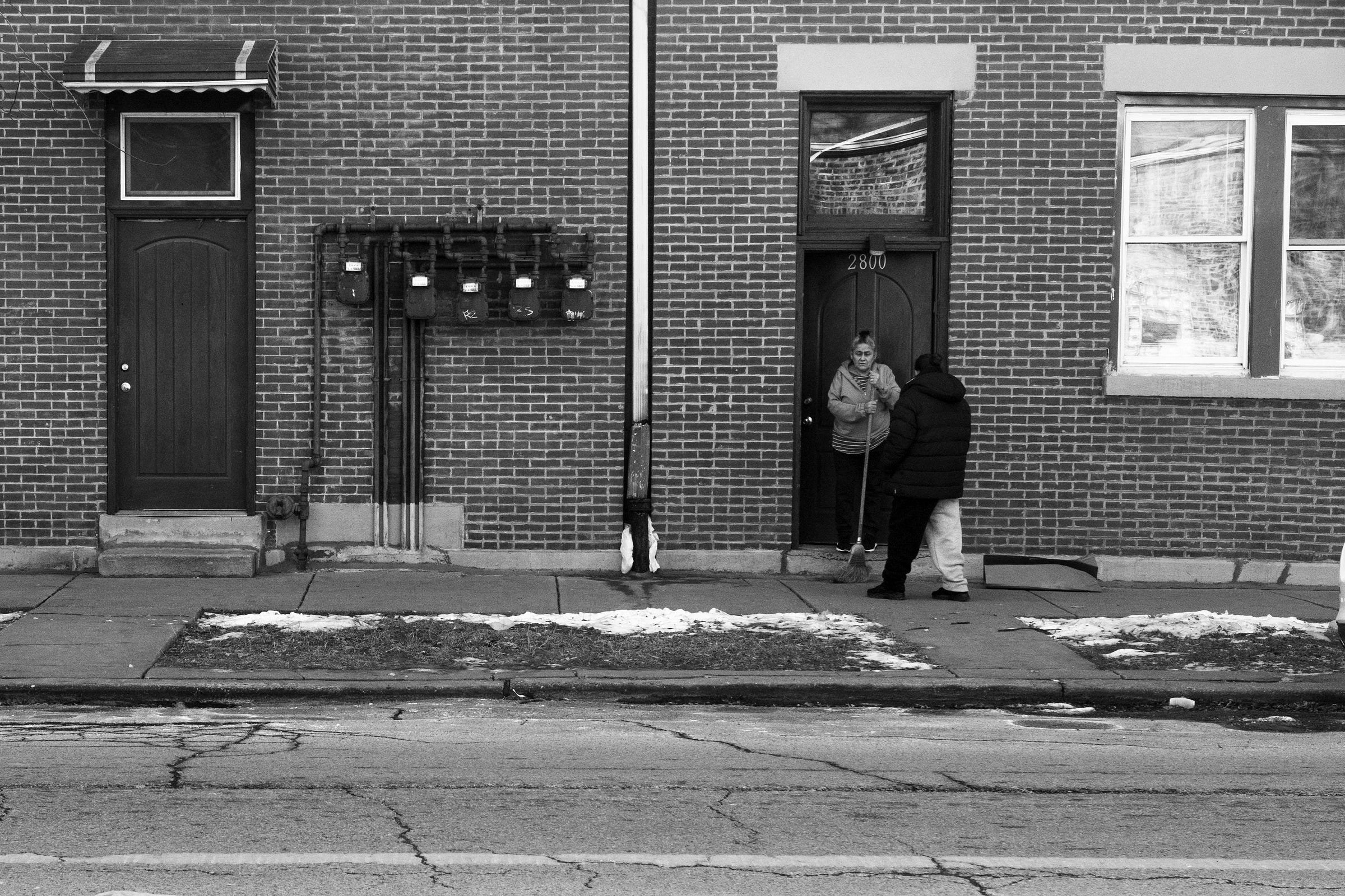 Black-and-white photo of woman talking on the street while one sweeps.