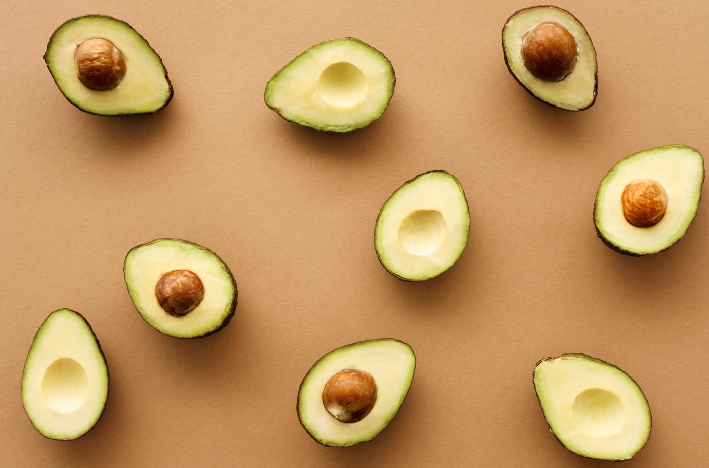 A flat lay of several halved avocados arranged on a neutral background, showing their bright green flesh and brown pits. Type Won Life™. A flat lay of several halved avocados arranged on a neutral background, showing their bright green flesh and brown pits. Type Won Life™.