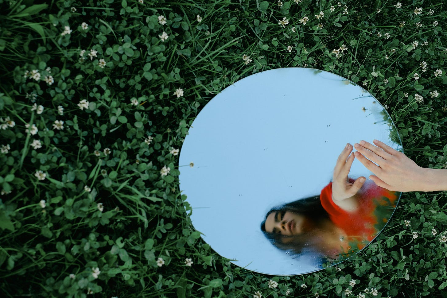 Woman looking into a mirror that is lying on a bed of clovers Woman looking into a mirror that is lying on a bed of clovers