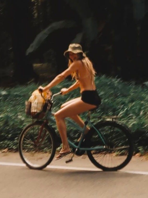 This may contain: a woman riding a bike down the street with a basket on it's back This may contain: a woman riding a bike down the street with a basket on it's back