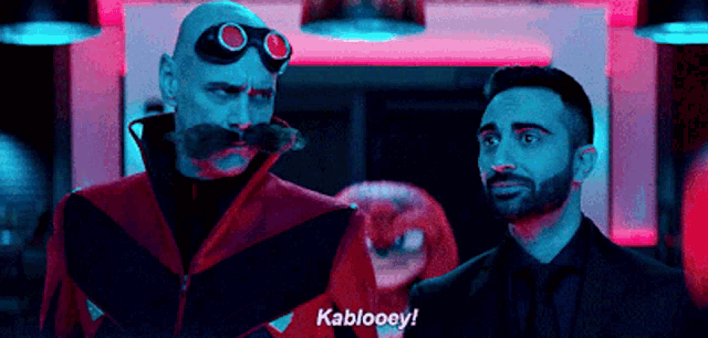 a man with a mustache and goggles is standing next to another man and says kablooey ! a man with a mustache and goggles is standing next to another man and says kablooey !