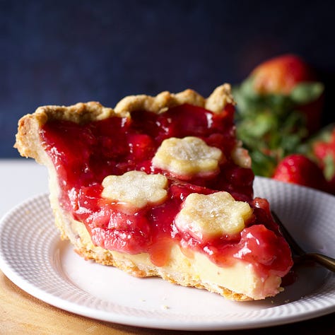 A raspberry cupcake on a plate, a slice of strawberry cream pie, and a slice of peach coffee cake.
