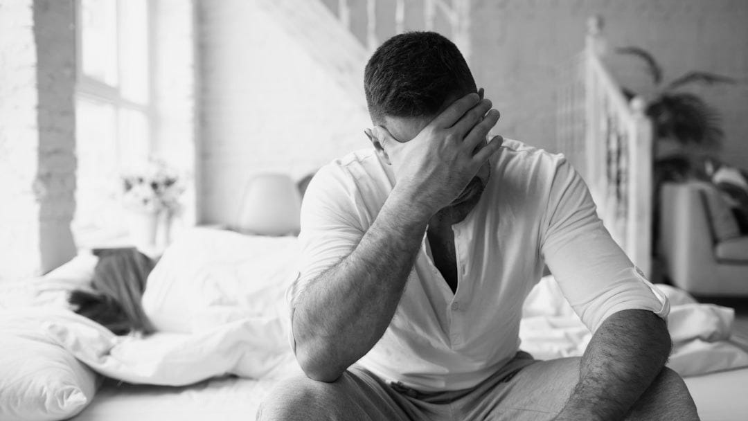 Man sitting on bed with hand over face