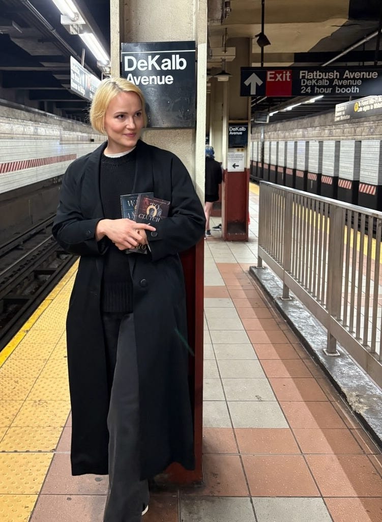 a blonde woman (me) leaning up against a pillar in a subway station in NYC, holding When Among Crows and To Clutch A Razor