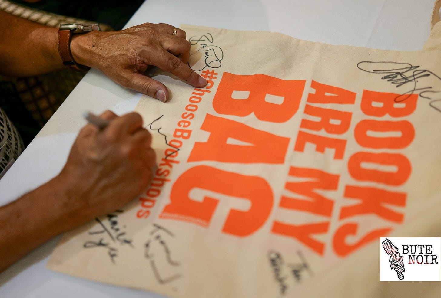 A pair of hands shown autographing a Books Are My Bag for Bute Noir