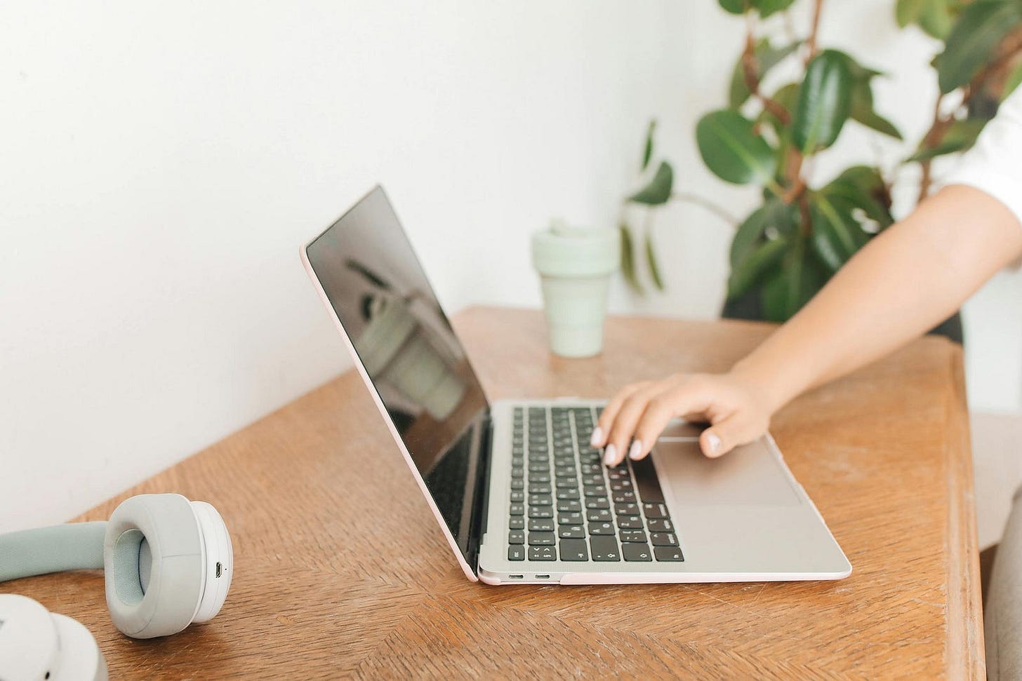 Woman freewriting on a laptop at a wooden desk, surrounded by plants and soft natural light — capturing stream-of-consciousness creativity, mindful surrender, and intentional digital journaling.