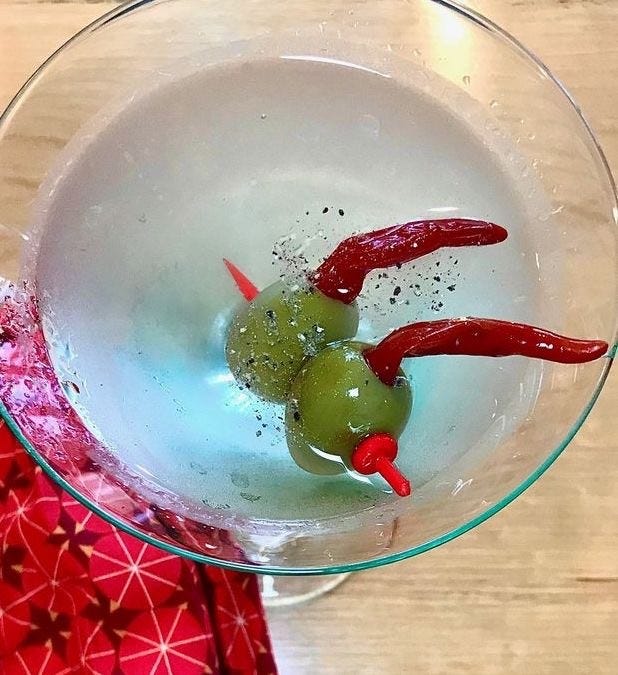 Photo of a martini glass with a cocktail and two olives with piri-piri peppers in them.