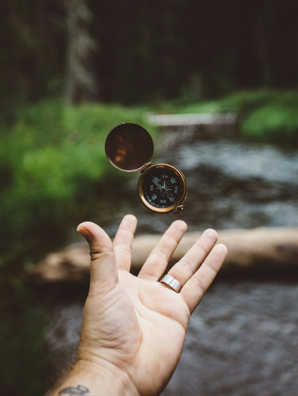 A person’s hand catching a compass in front of an out-of-focus riverbed. A person’s hand catching a compass in front of an out-of-focus riverbed.