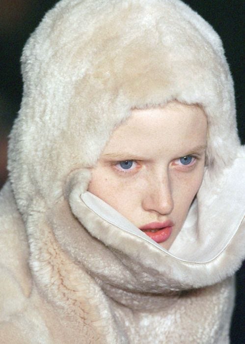 This may contain: a woman with blue eyes wearing a white fur coat over her head and scarf around her neck