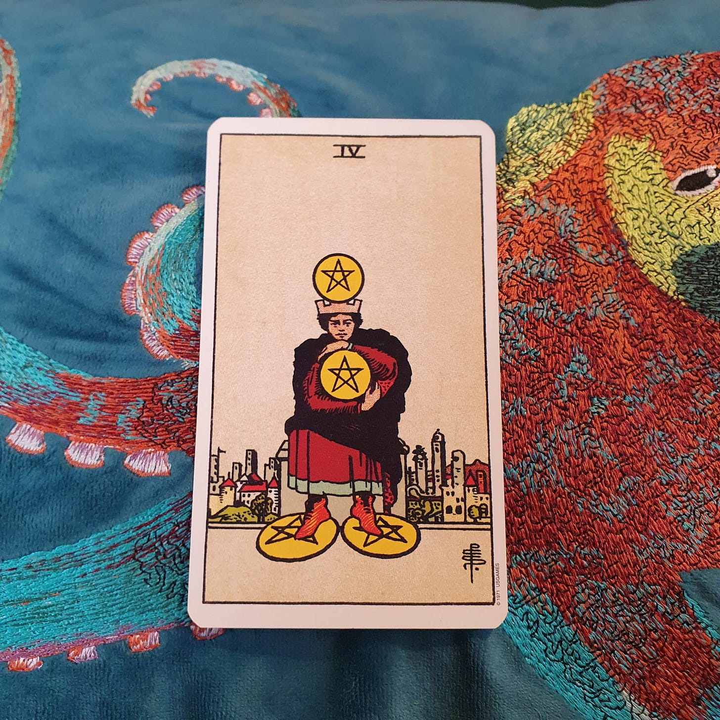 Four of Pentacles tarot card from a Rider-Waite-Smith style deck on blue embroidered fabric for Tarot DMs.