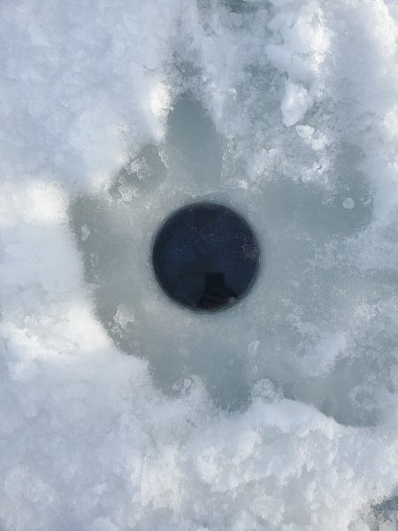 a circle drilled through ice revealing dark water below