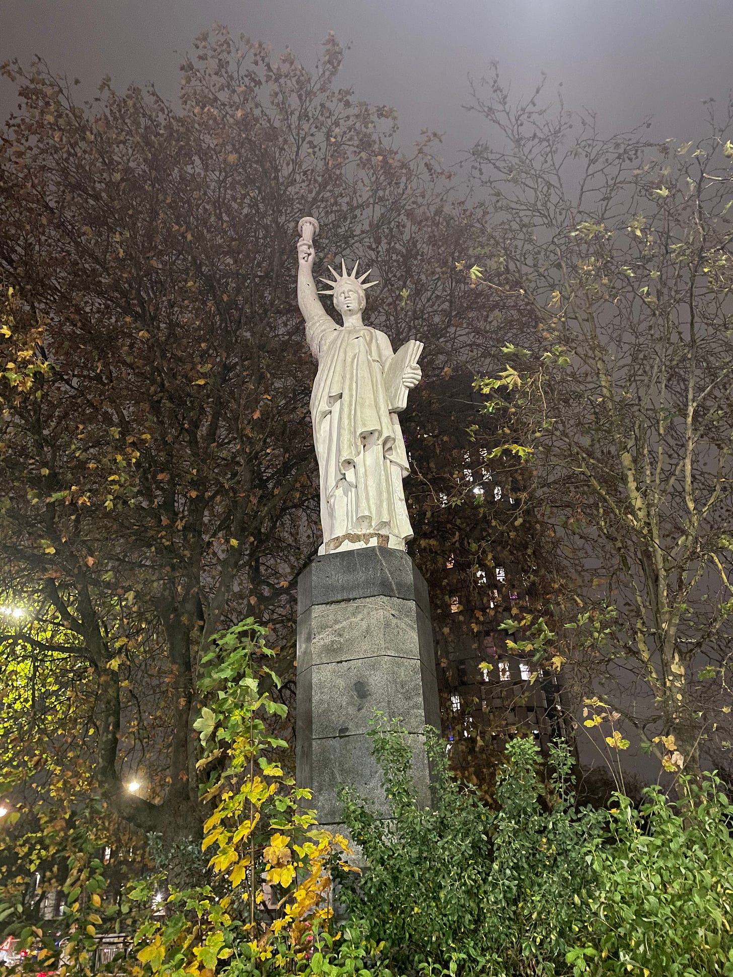 A smaller version of the Statue of Liberty, against a backdrop of leafless trees, in the rain.