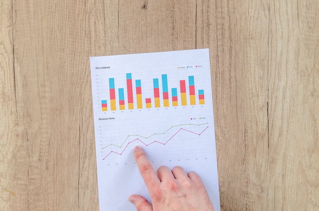 How to build wealth A hand points to colorful business charts and graphs on a paper sheet on a wooden desk.