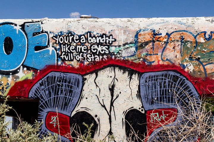 The first image shows an old store front with the word "EAT" in red block letters on a building with graffiti and a palm tree blowing behind it. The second image depicts graffiti that reads "You're a bandit like me, eyes full of stars" above a painting of a bison skull outlined in red.