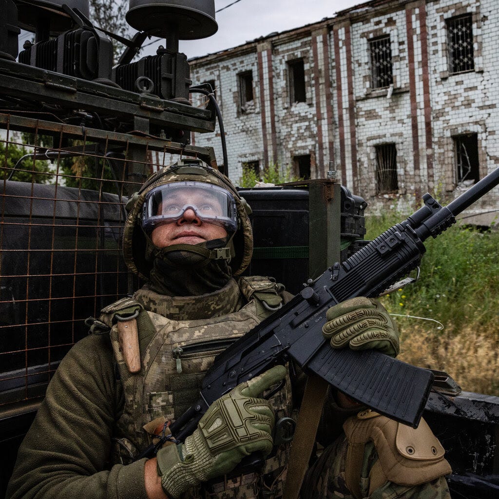 A soldier in fatigues holds a rifle and looks up at the sky. 