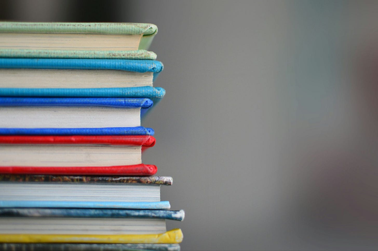 Stock photo of a stack of colorful schoolbooks against a blurred grey background. All that's visible of the books is their pages and colorful bindings.