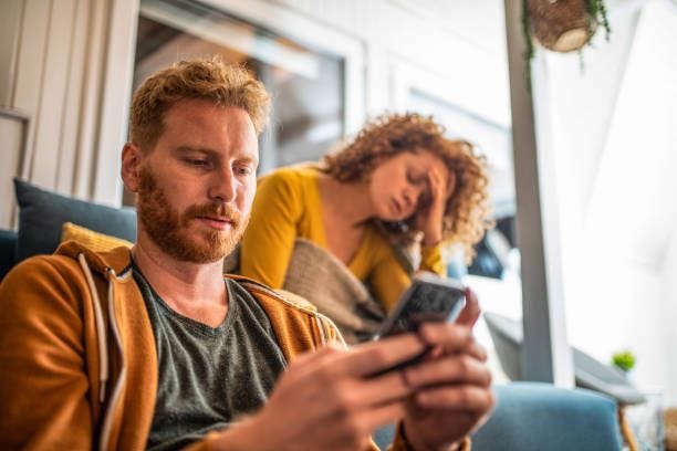 young man ignoring his girlfriend while using phone. - woman on phone ignoring man stock pictures, royalty-free photos & images