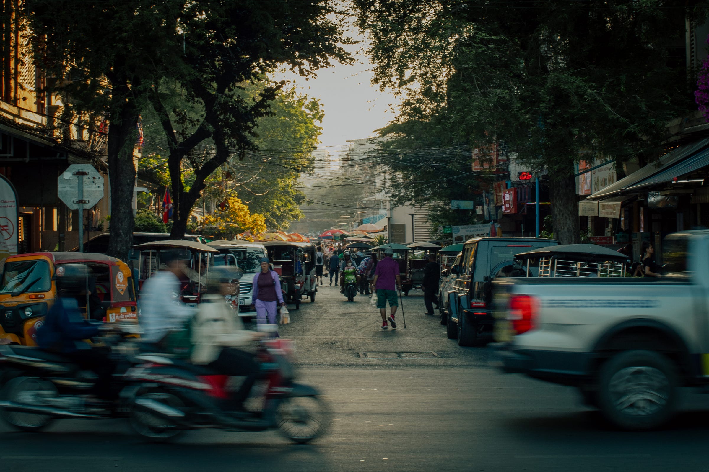 Rue animée à Phnom Penh, au Cambodge, avec des tuk-tuks, des motos et des piétons à l’heure dorée, capturant la vie quotidienne et le mouvement de la ville.