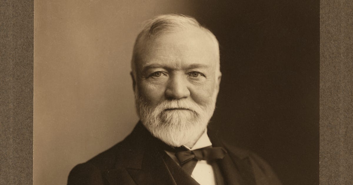 A black and white photograph of a white man in his sixties with a full white beard and white combed hair. He’s visible from the shoulders up with a tuxedo.