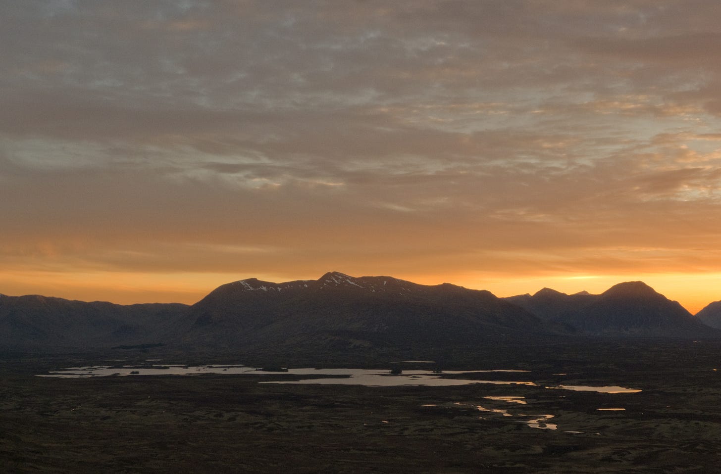 yellow sunset behind hills, lake in foreground