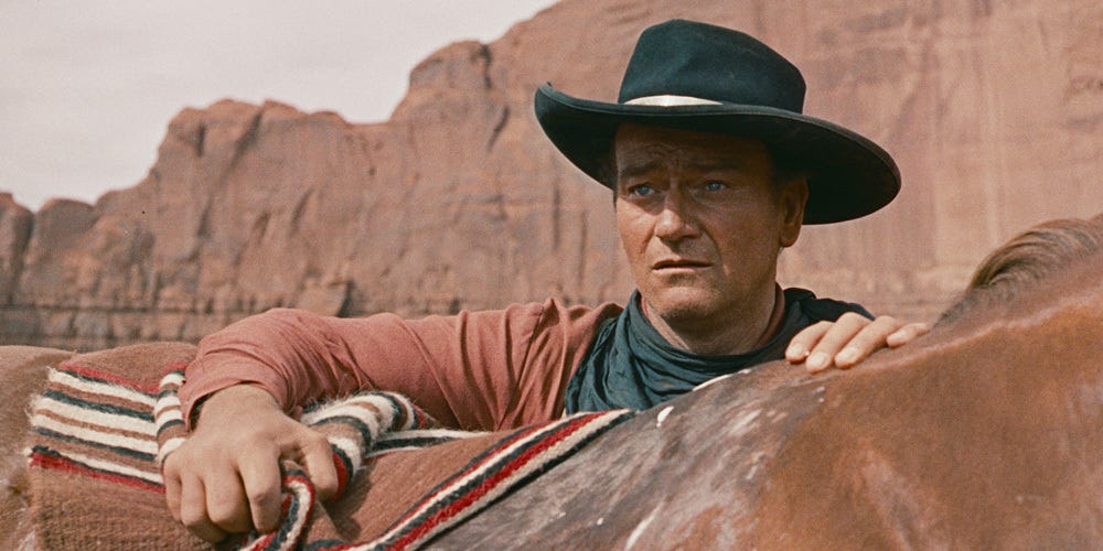 John Wayne in a hat looking over the back of his horse (horse head is off camera)