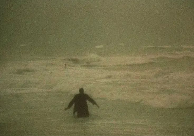 This may contain: a man wading in the ocean on a foggy day